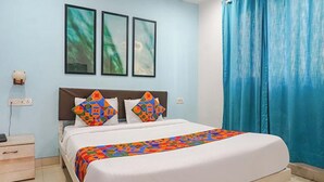 Une chambre d’hôtel avec un lit, deux oreillers, une table de chevet, une prise de courant et un rideau bleu.