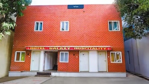 Un bâtiment en briques rouges sur lequel on peut lire l’inscription « HÔTEL GALAXY, SERVICE D’HÔTELLERIE ». La façade comporte quatre portes blanches et deux fenêtres.