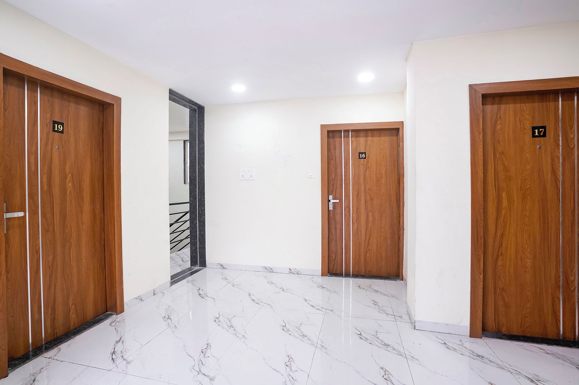 Un pasillo con tres puertas de madera, cada una con un número. El piso está cubierto de mármol blanco.