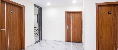 Un pasillo con tres puertas de madera, cada una con un número. El piso está cubierto de mármol blanco.