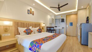 Habitación de hotel con cama, mesita de noche, lámpara, ventilador de techo y un área de kitchenette.