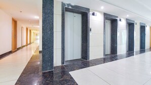 Un largo pasillo con suelo de mármol, puertas e iluminación empotrada en el techo.