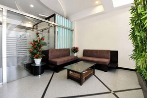 A modern lobby with two sofas, a glass coffee table, a potted plant, and a striped wall. - FabHotel Harsh Paradise - Malviya Nagar (Jaipur)