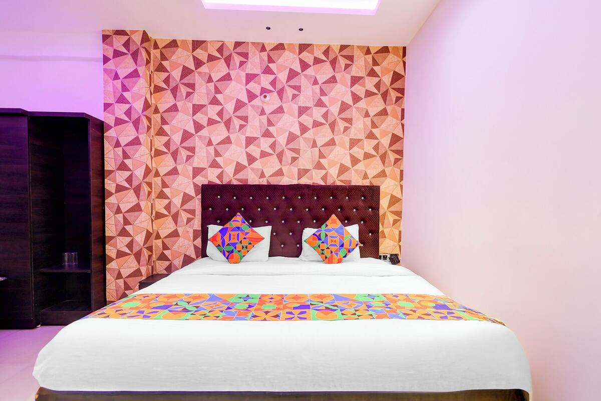 A bedroom with a geometric patterned wall, a tufted headboard, and a colorful bedspread.