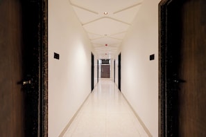 A long, narrow hallway with white walls and a tiled floor, leading to a staircase. - FabHotel Royal Residency - Nr. Barra World Bank Crossing (Kanpur)
