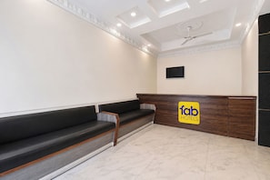 A hotel reception area with a wooden reception desk, a black sofa, and a ceiling fan. - Fabhotel Deep (Jaipur)