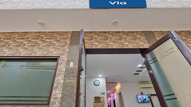 Entrada de un edificio con fachada de piedra, una señal de Via, un reloj y una pantalla de televisión.