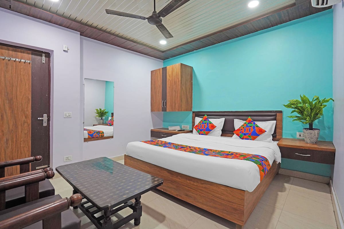 A bedroom with a bed, a wooden nightstand, a small table, a ceiling fan, and a potted plant.