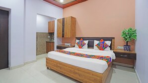Un dormitorio con cama de madera, una mesita de noche, una planta en maceta y una pequeña cocina.