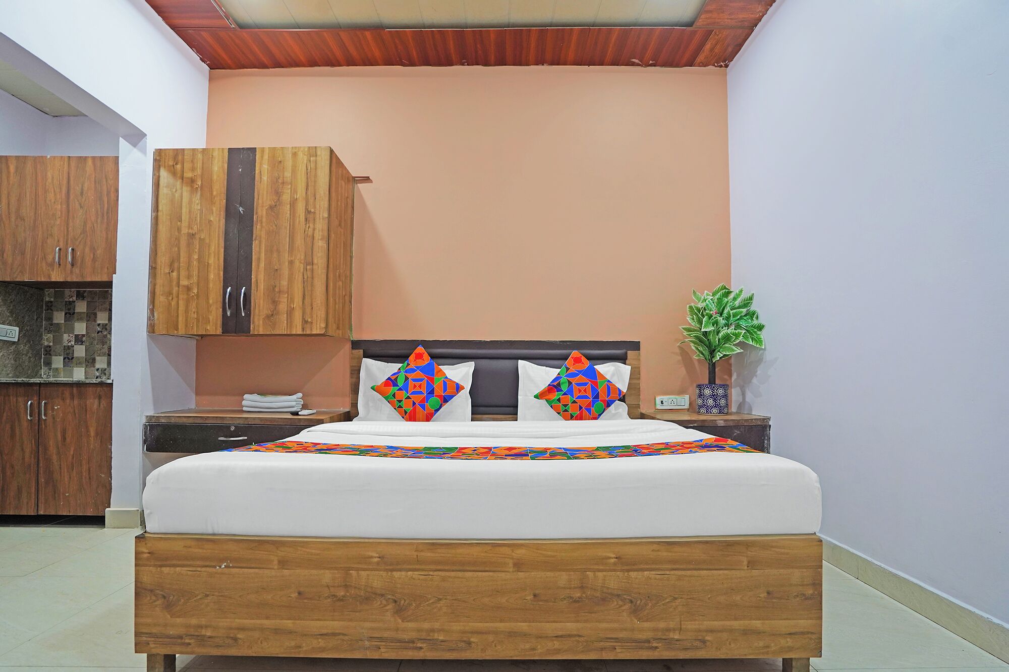 A bedroom with a wooden bed frame, a nightstand, a potted plant, and a wardrobe.