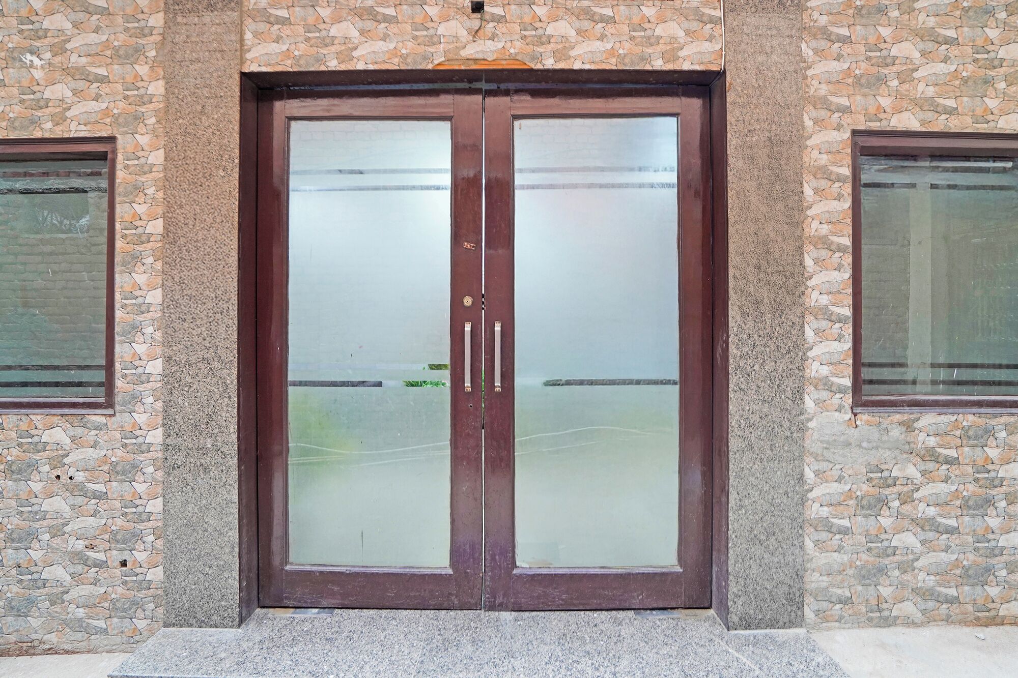 A double door with frosted glass panels, set in a stone wall with two windows on either side.