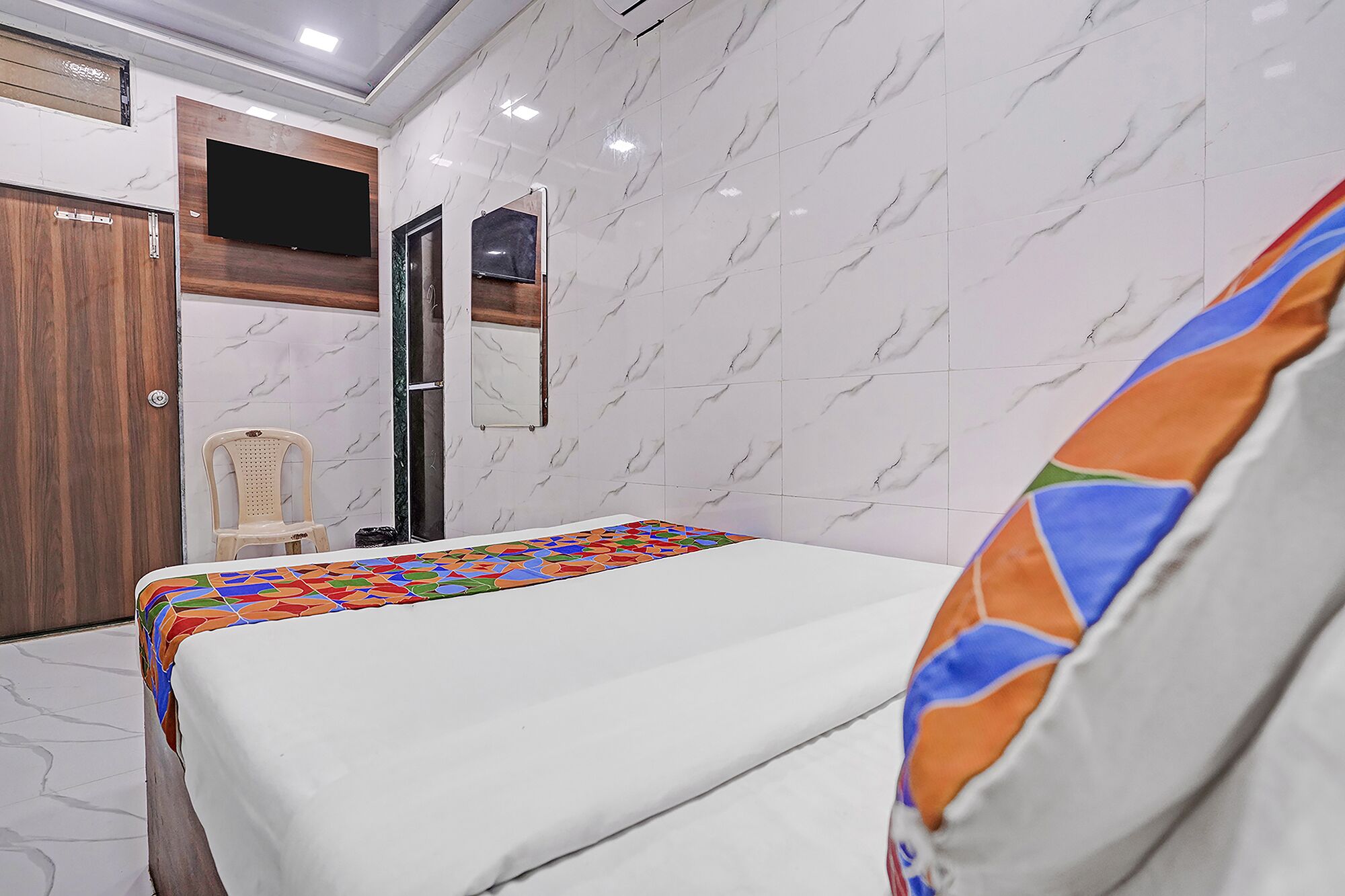 Una camera d'albergo con un letto, una sedia, una TV e uno specchio.