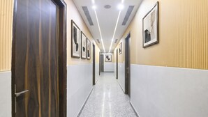 A hallway with framed artwork on the walls, a polished floor, and a door on the left. - FabHotel D Crown - Nr Ashok Vihar (New Delhi)