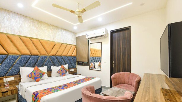 A hotel room with a bed, a pink armchair, a wooden table, a ceiling fan, and an air conditioning unit. - FabHotel D Crown - Nr Ashok Vihar (New Delhi)