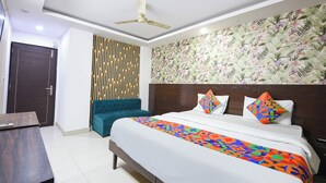 Une chambre d’hôtel comprenant un lit, un bureau, une chaise, un ventilateur de plafond et un mur orné d’un motif floral.