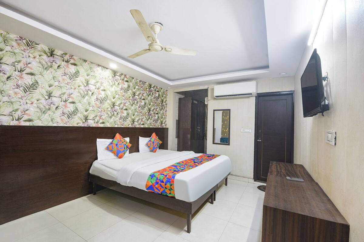 A hotel room with a bed, a desk, a ceiling fan, a TV, and a shower door.