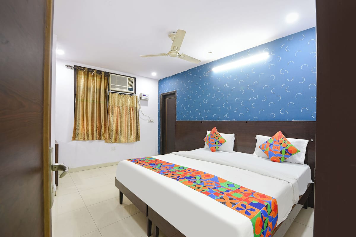 A hotel room with a bed, a ceiling fan, a window with curtains, and a wall with a pattern.