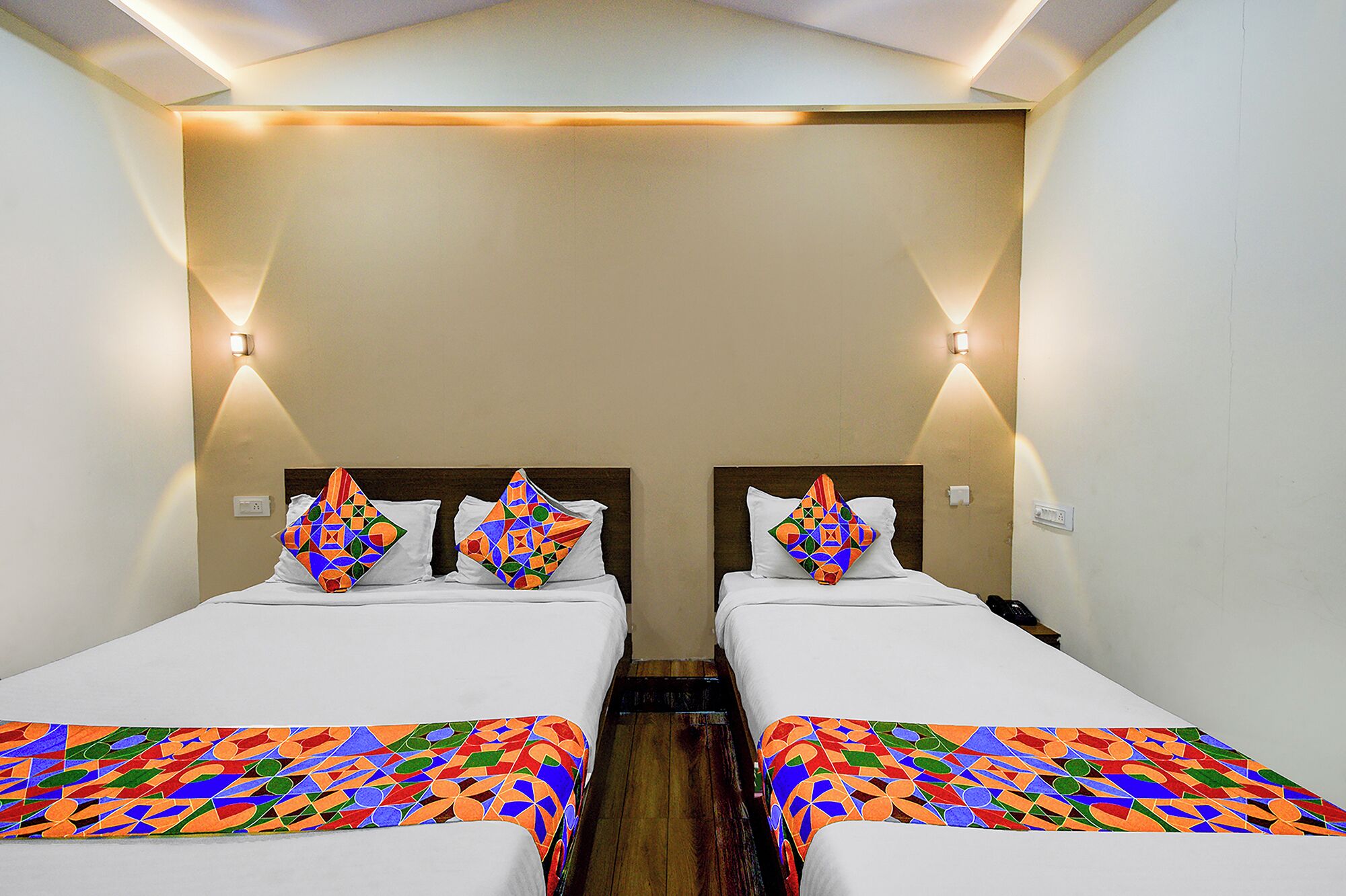 Habitación de hotel con dos camas, cada una con una colcha de diseño geométrico y colores vivos, almohadas blancas y suelo de madera.
