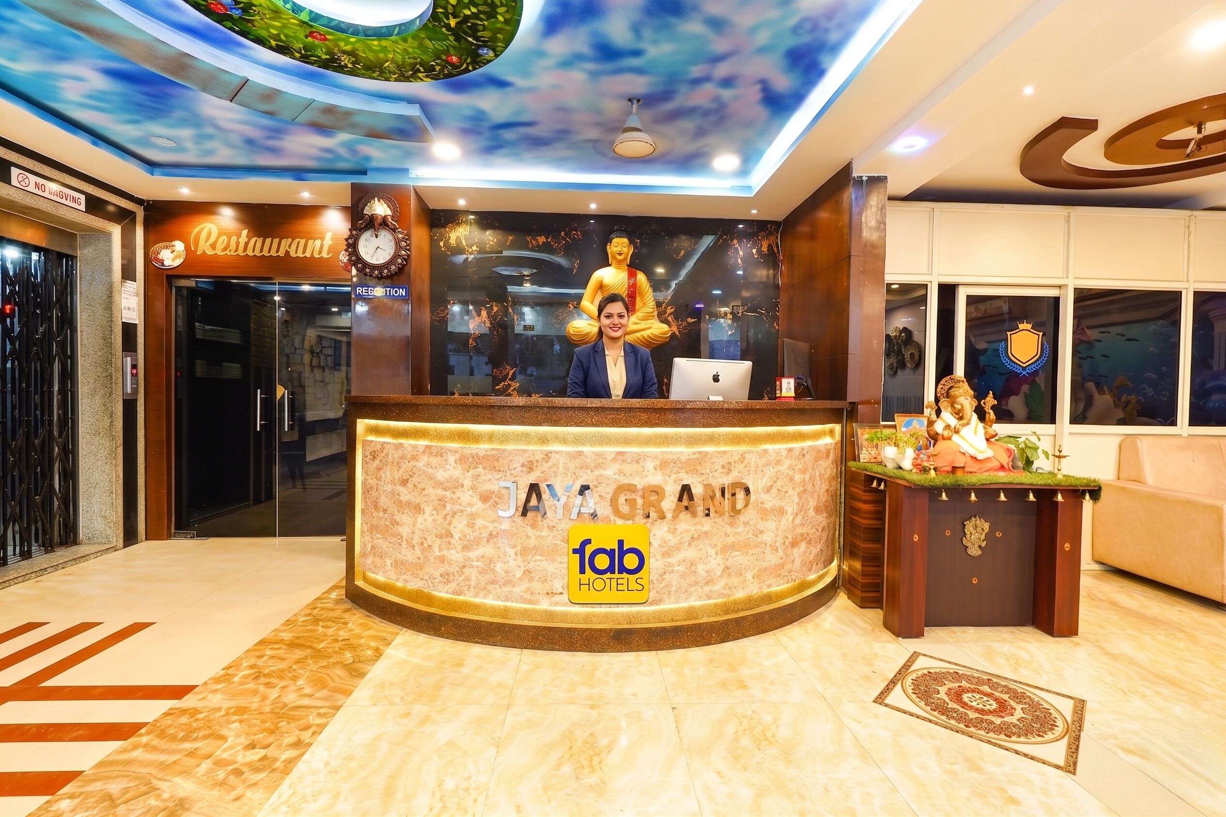 A reception desk with a Buddha statue, a clock, and a sign for 'JAYA GRAND FAB HOTELS.'