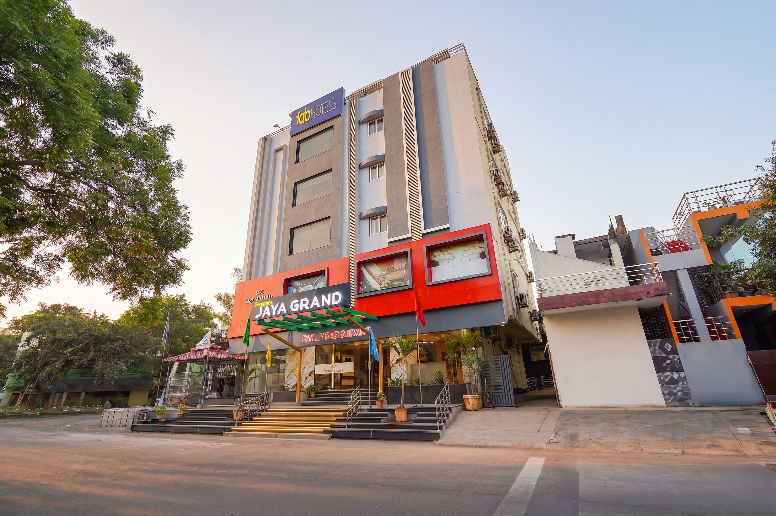 A multi-story building with a prominent 'JAYA GRAND' sign, a staircase leading to the entrance, and a flagpole with a flag.