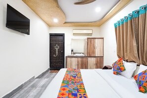 Un dormitorio con cama, televisor montado en la pared, armario de madera y baño con espejo y lavamanos.