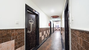A hallway with tiled walls, a wooden floor, and doors with a crown symbol. - FabHotel Jaya Grand - Nr. Railway Station (Guntur)