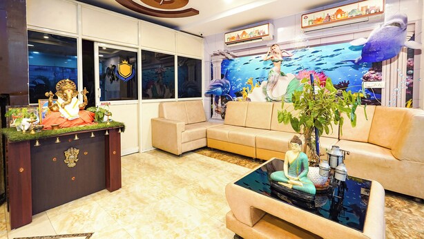 A modern living room with a sofa, a coffee table with a Buddha statue, a decorative cabinet with religious items, and a mural of an underwater scene. - FabHotel Jaya Grand - Nr. Railway Station (Guntur)