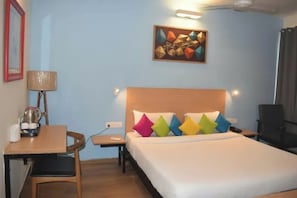 Ein Hotelzimmer mit Bett, Schreibtisch, Stuhl, Lampe, einem Gemälde und einem Fenster.