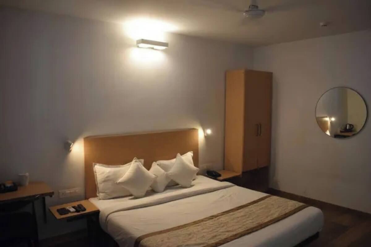 Ein Hotelzimmer mit Bett, Nachttisch, Lampe, Kleiderschrank und einem runden Spiegel an der Wand.