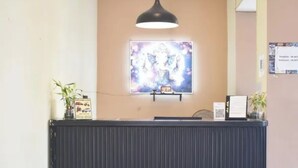 A reception desk with a framed artwork above it, a black pendant light, and a small shelf with a framed picture and a plant. - FabHotel Prime Plaza Inn - 800M From Calangute Beach (Calangute)