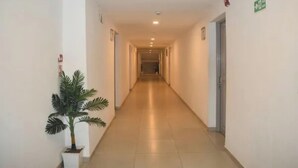 A long, narrow hotel corridor with a potted plant on the left, doors on both sides, and a green exit sign on the right. - FabHotel Prime Plaza Inn - 800M From Calangute Beach (Calangute)