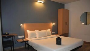 A hotel room with a bed, a desk, a chair, a wardrobe, and a mirror. - FabHotel Prime Plaza Inn - 800M From Calangute Beach (Calangute)