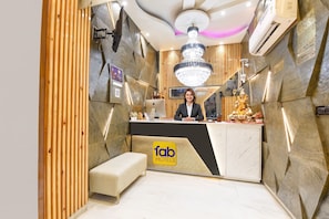 A reception desk with a chandelier, a wooden panel wall, and a bench. - Fabhotel Dev Palace II (New Delhi)