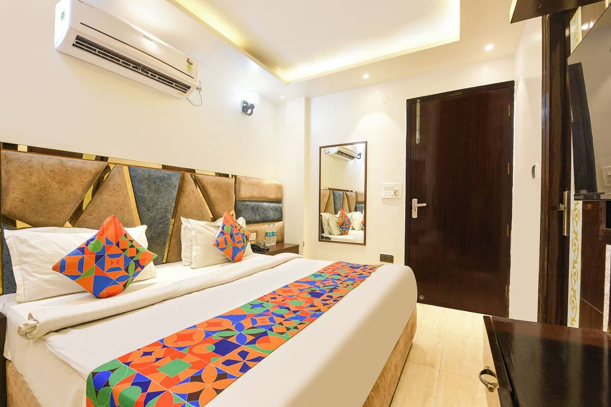 Una habitación de hotel con cama, mesita de noche, aire acondicionado, espejo y puerta.