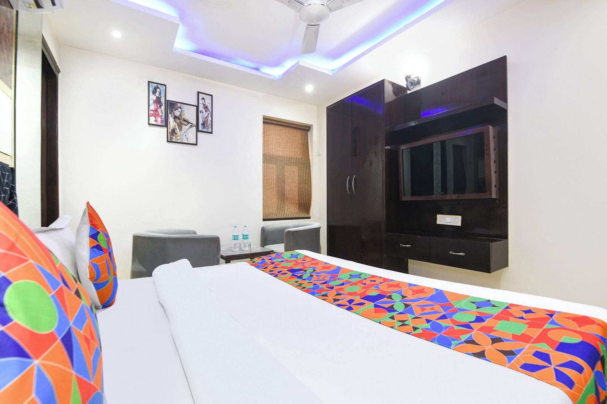 A hotel room with a bed, a TV, a wardrobe, a desk, and a window with curtains.
