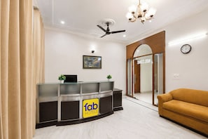 A hotel reception area with a glass desk, a ceiling fan, a chandelier, a sofa, and a clock on the wall. - FabHotel The Arjun Sushant lok - Iffco Chowk Sector 29 (Gurugram)