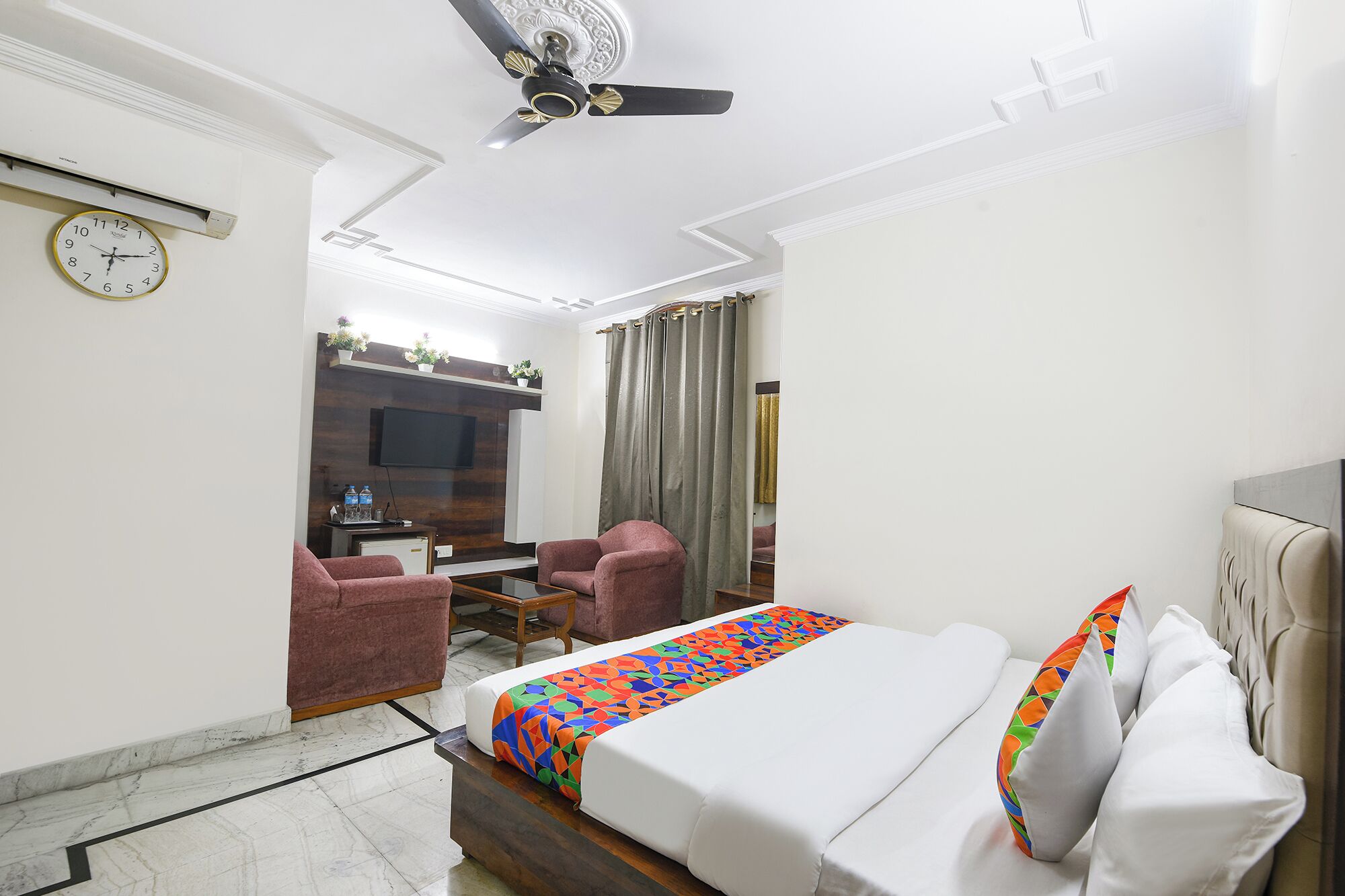 A hotel room with a bed, a desk, a chair, a TV, and a ceiling fan.