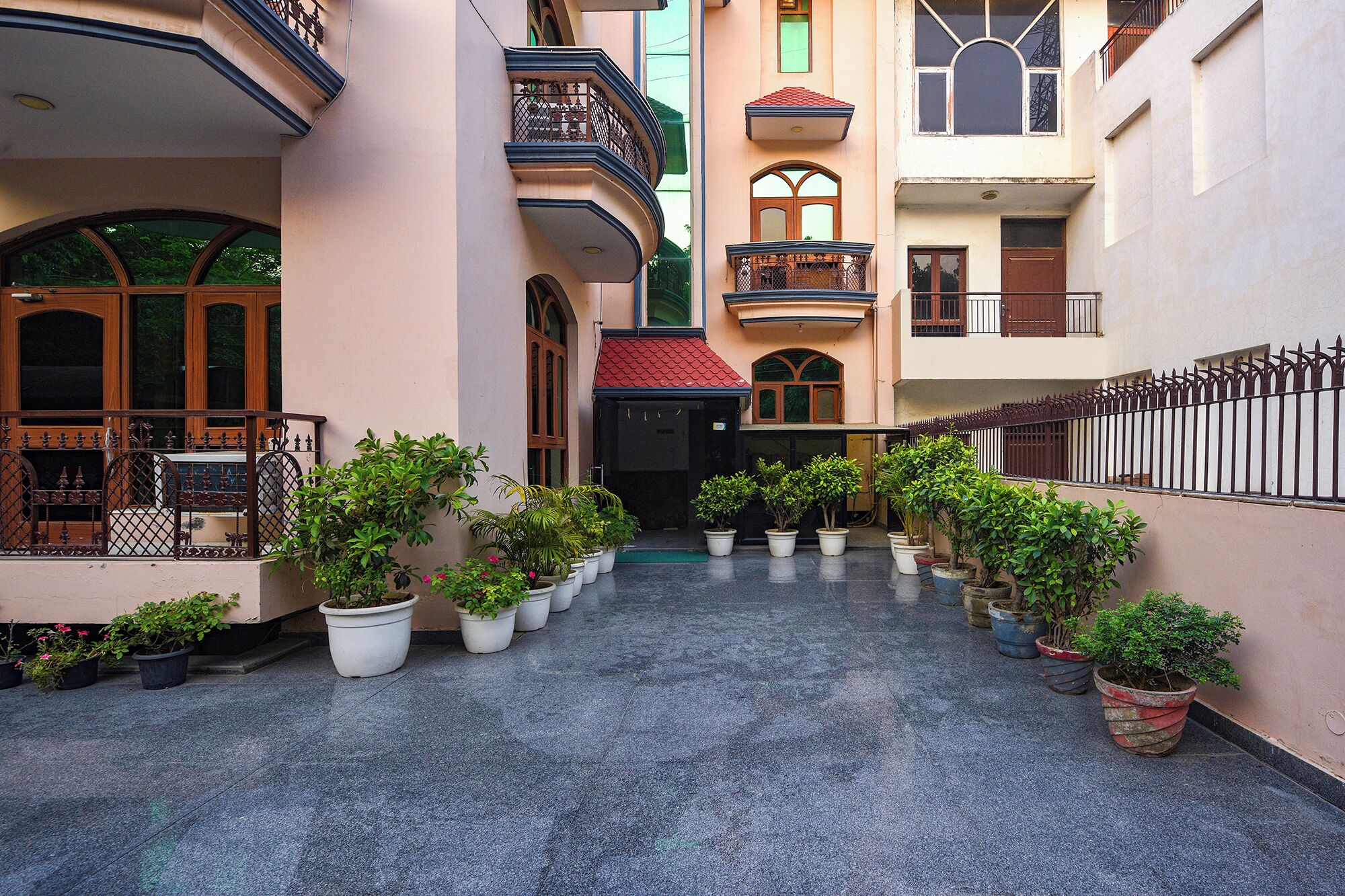 A courtyard with potted plants, a red-roofed entrance, and a metal fence.