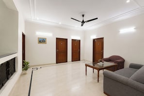 A spacious room with a ceiling fan, three wooden doors, a grey sofa, a small table, and a potted plant. - Fabhotel The Arjun (Gurugram)