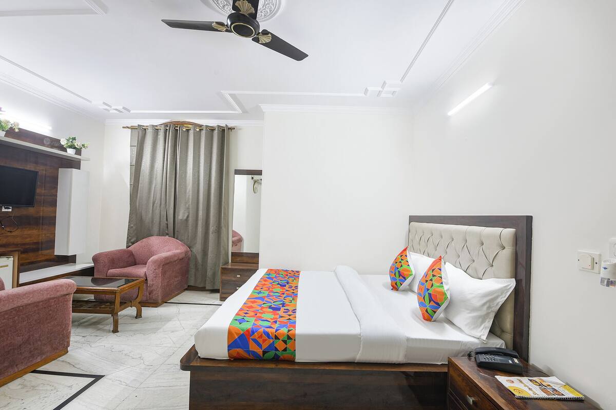 Ein Hotelzimmer mit Bett, Schreibtisch, Sessel, Fernseher und Deckenventilator.