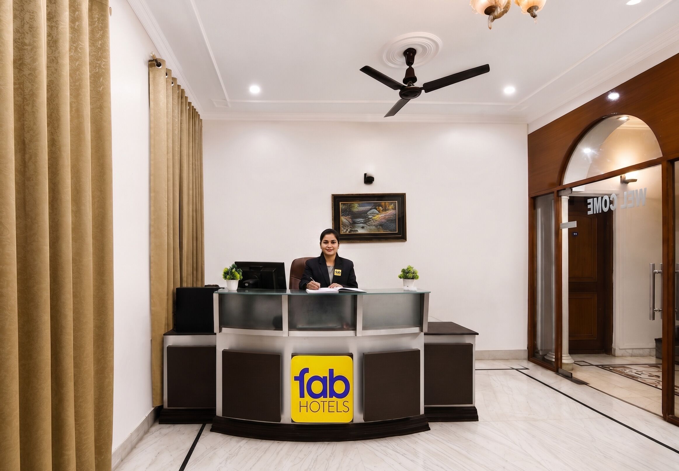 A reception desk with a logo, a ceiling fan, a framed picture, and a door labeled 'MELECOME'.