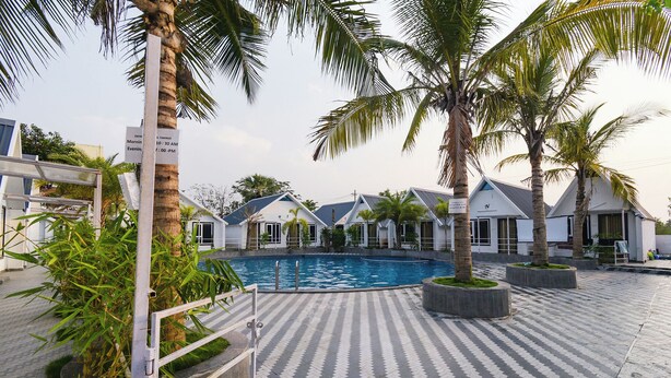 A swimming pool surrounded by palm trees and a tiled walkway. - Fabhotel Sunshine (Yadagirigutta)