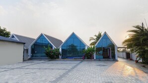 A modern building with a paved courtyard, large glass windows, and a triangular roof design. - Fabhotel Sunshine (Yadagirigutta)