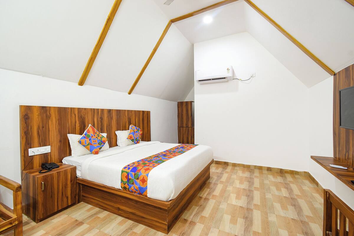 Une chambre avec une tête de lit en bois, un lit agrémenté de coussins colorés, une table de chevet avec un téléphone et un téléviseur placé à droite.