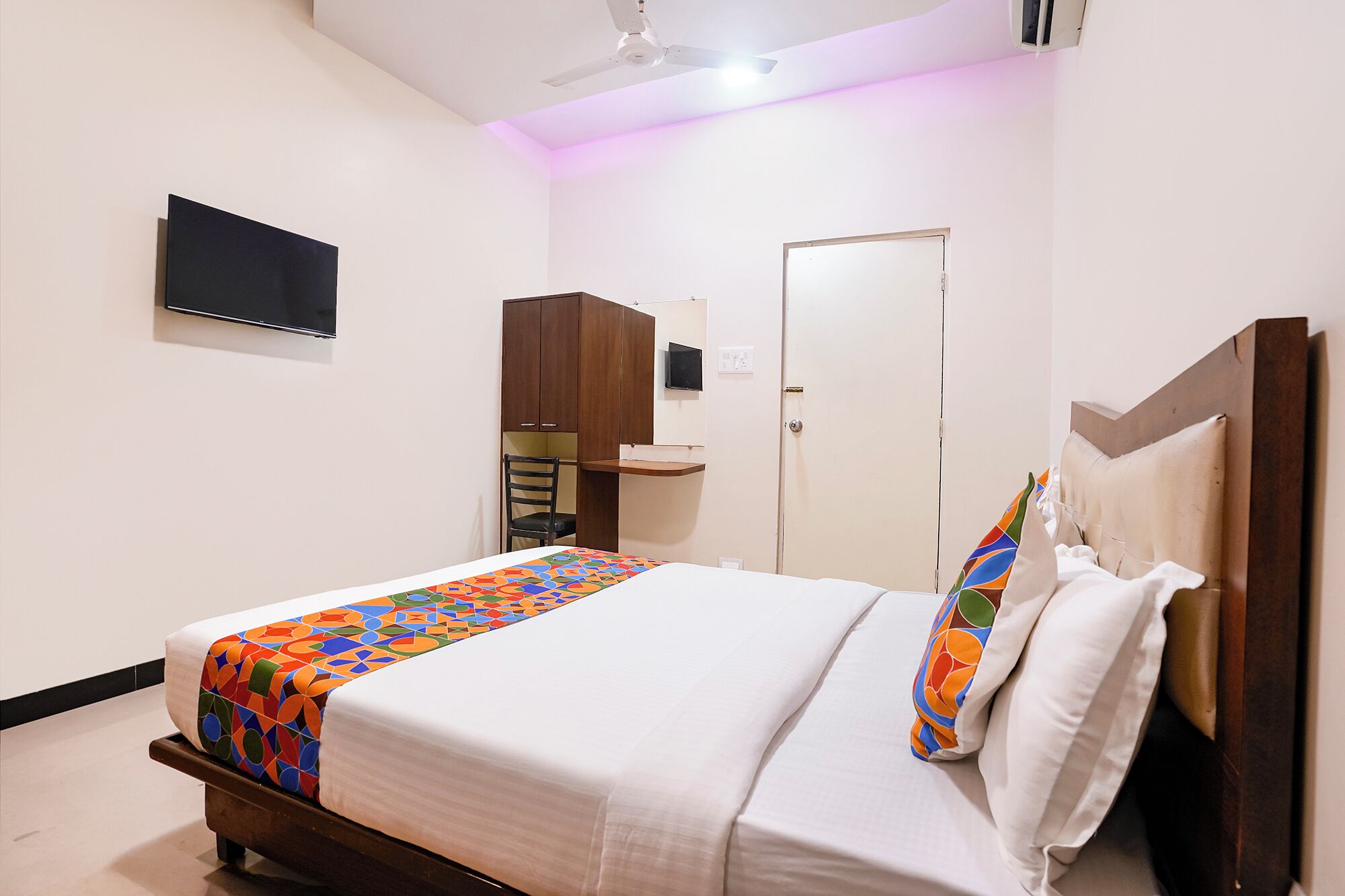 Un dormitorio con cama, televisor montado en la pared, armario y una puerta.