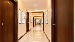 A hotel hallway with wooden doors, framed artwork on the walls, and a shiny tiled floor. - Fabhotel Sk Galaxy (Thane)