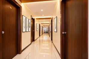 Un pasillo de hotel con puertas de madera, obras de arte enmarcadas en las paredes y un suelo de baldosas brillantes.