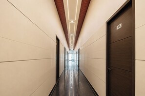 A long, narrow hallway with a reflective floor, a wooden door on the right, and a number sign above it. - Fabhotel Metro Inn I (New Delhi)