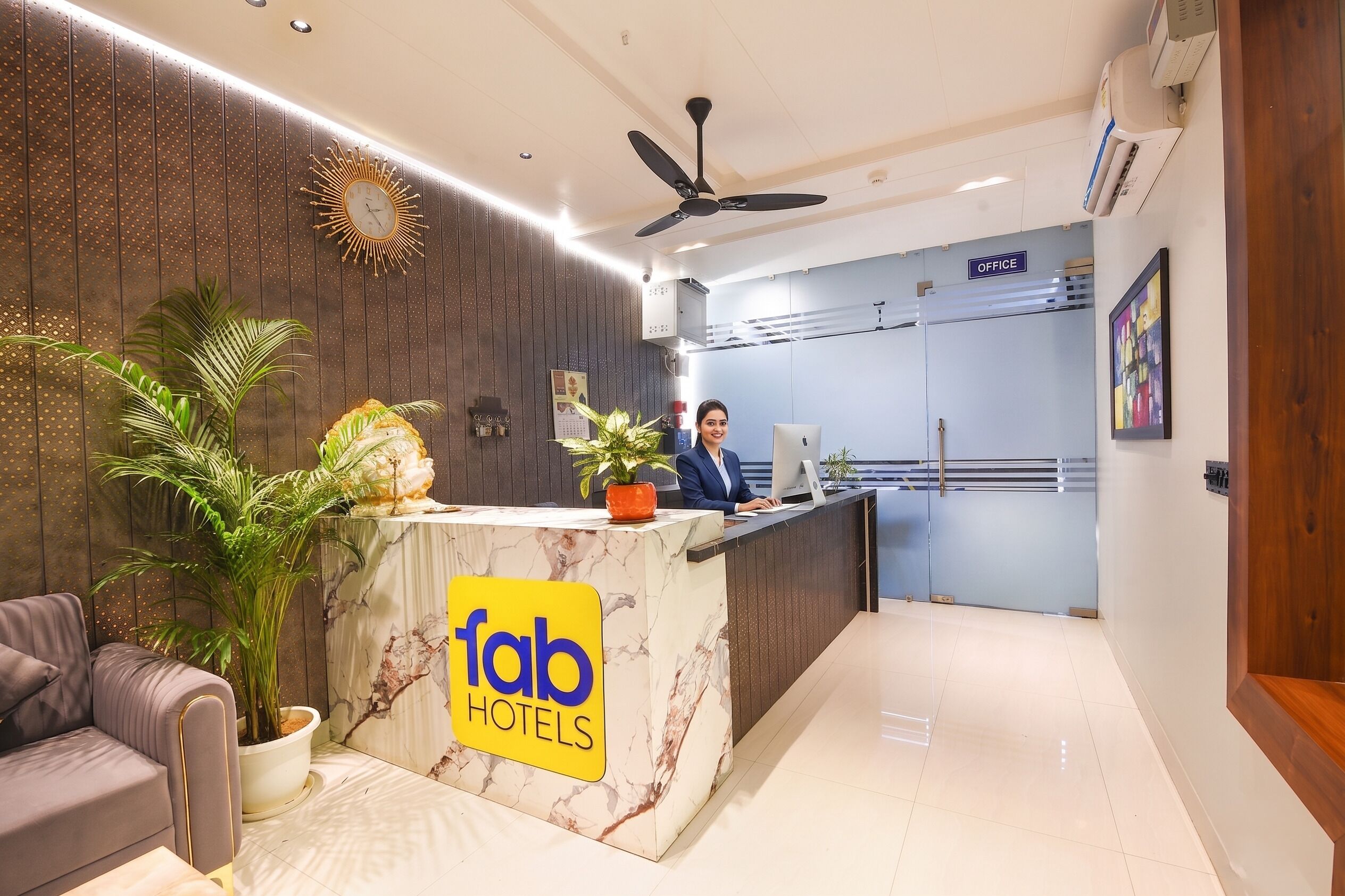 Uma área de recepção de hotel com balcão de mármore, um recepcionista e uma placa com a inscrição 'fab hotels'.