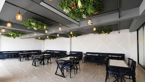 Un vaste espace dédié à la salle à manger, doté de hauts plafonds, de plantes suspendues et d’un éclairage moderne en suspension.